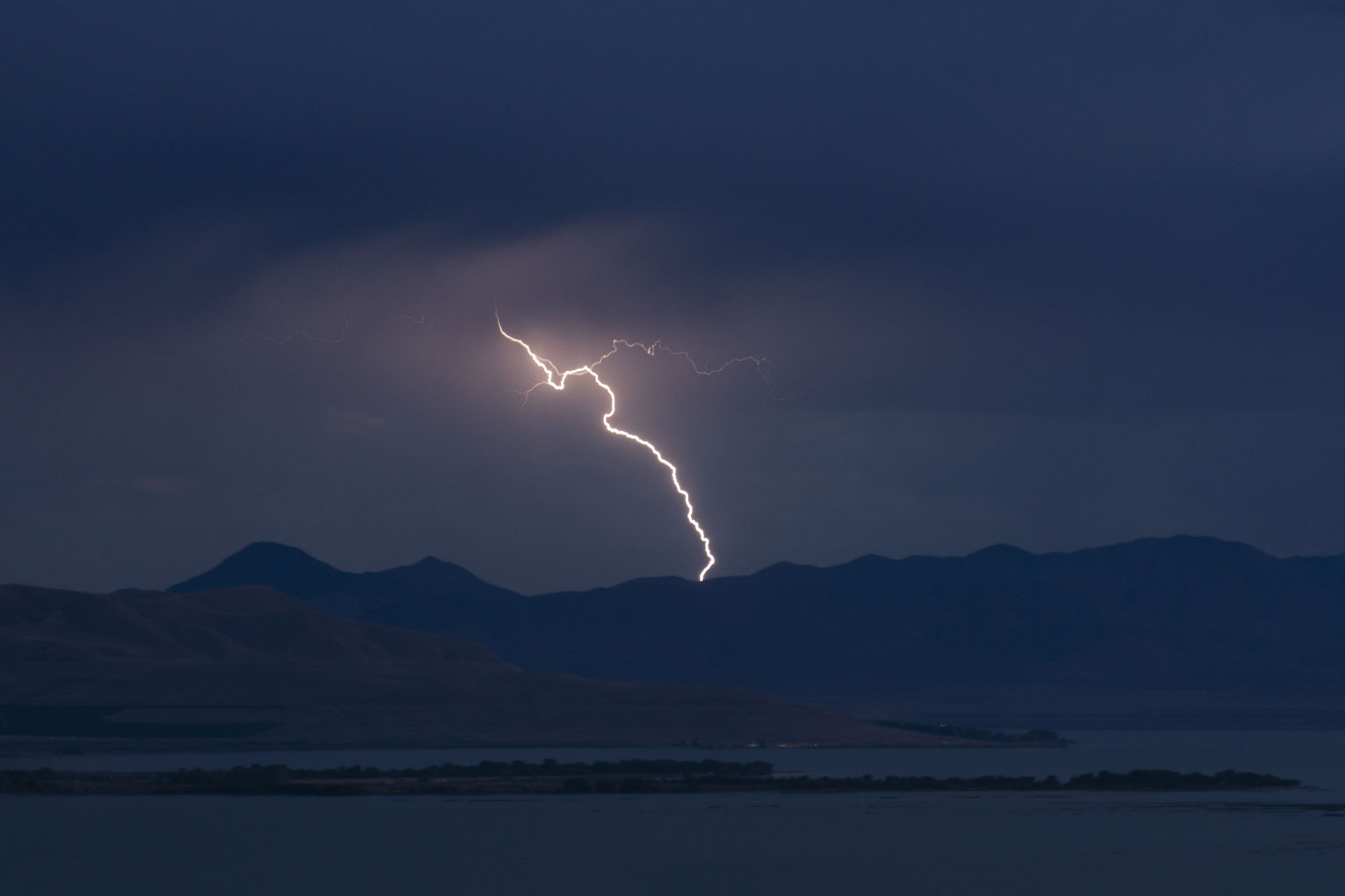 In the darkening blue sky a single diagonal bolt follows the swish of the lit rain mist